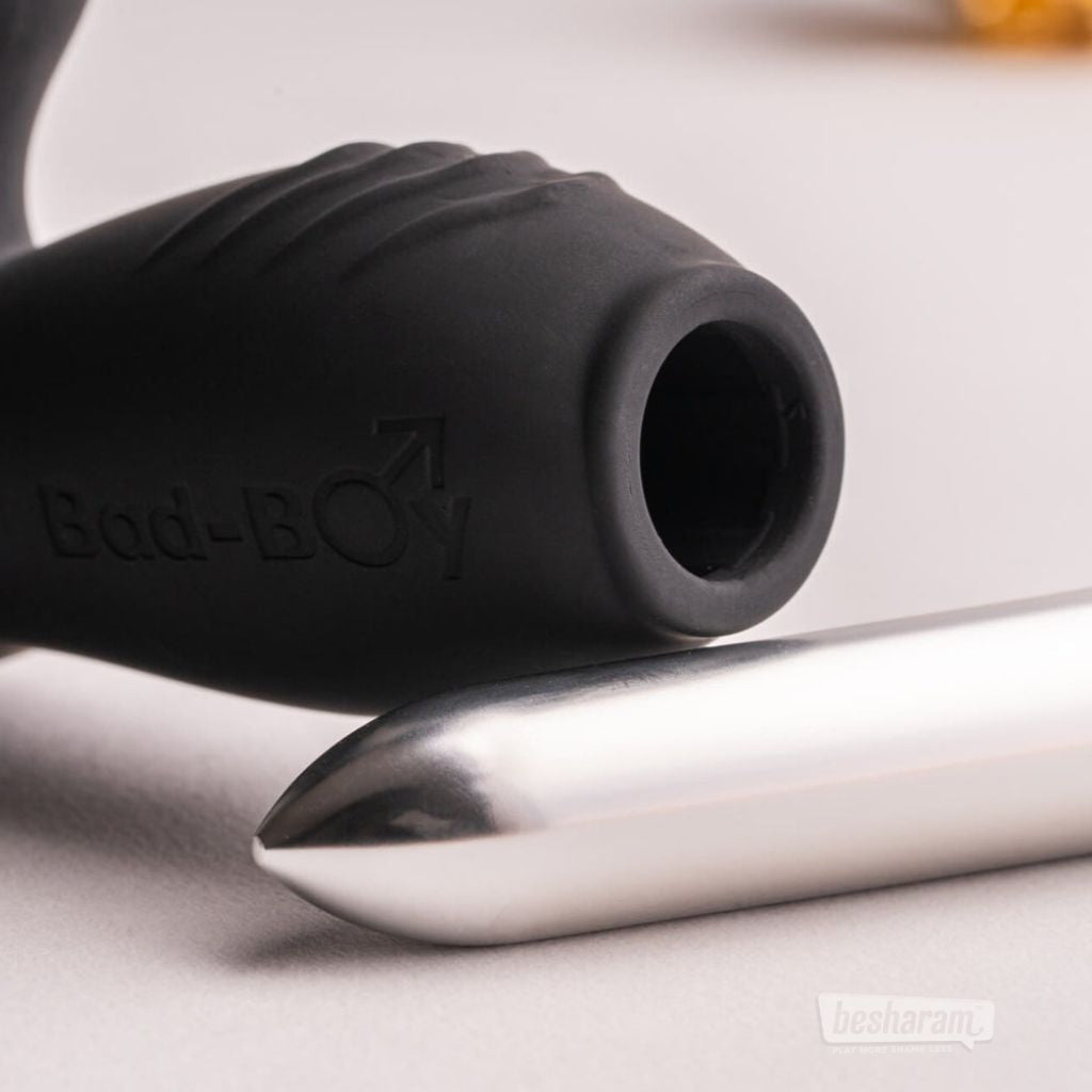 Close-up detail of a black Bad-Boy prostate massager with a silver bullet vibrator placed beside the sleeve opening.