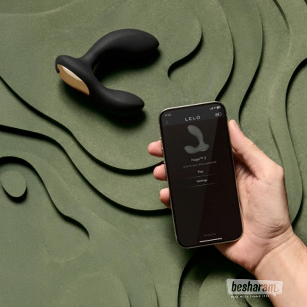 Hand holding a phone with the LELO app next to the Hugo 2 prostate massager on a textured green surface