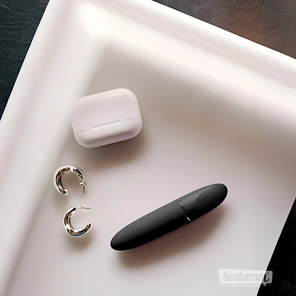 LELO Mia 3 compact bullet vibrator in black placed on a white tray with earbuds and earrings, minimalist flat lay lifestyle image