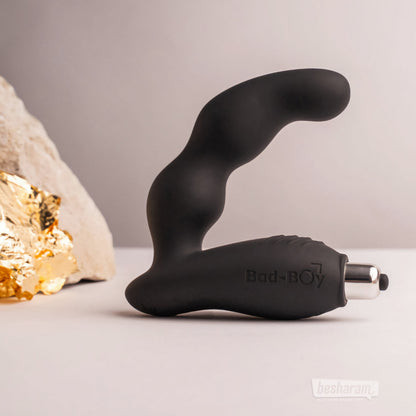The black Bad-Boy prostate massager standing upright on a neutral backdrop with decorative stones and gold textures.