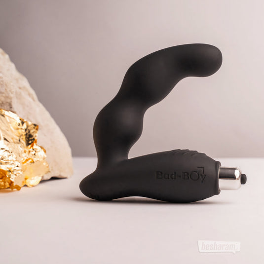 The black Bad-Boy prostate massager standing upright on a neutral backdrop with decorative stones and gold textures.