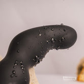 Close-up of the curved black Bad-Boy prostate massager with water droplets highlighting its waterproof silicone surface.
