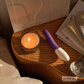 LELO LIV 3 Plum vibrator on a bedside table next to a lit candle and books