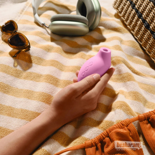 Hand holding the LELO Sona 2 Travel pink clitoral massager on a striped towel