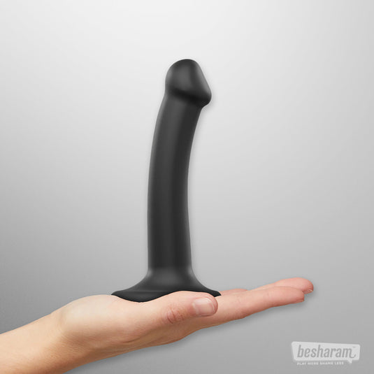 Black strap on dildo standing on open hand for size reference, smooth silicone bendable dildo