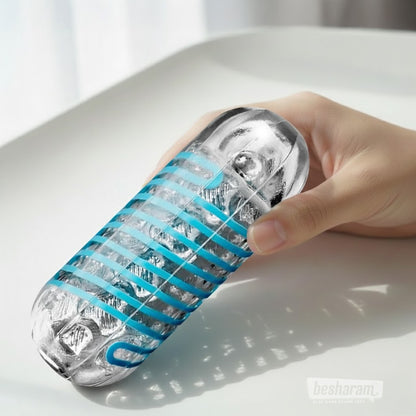 Hand holding a clear textured male masturbator sleeve with blue grip bands on a white surface for product display